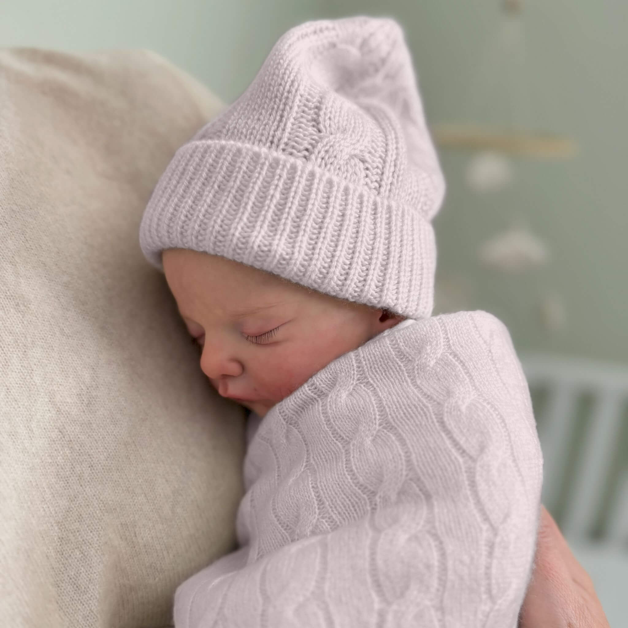 Newborn baby wrapped in a pink cable knit blanket, wearing a pink cable knit hat, cuddled by mother