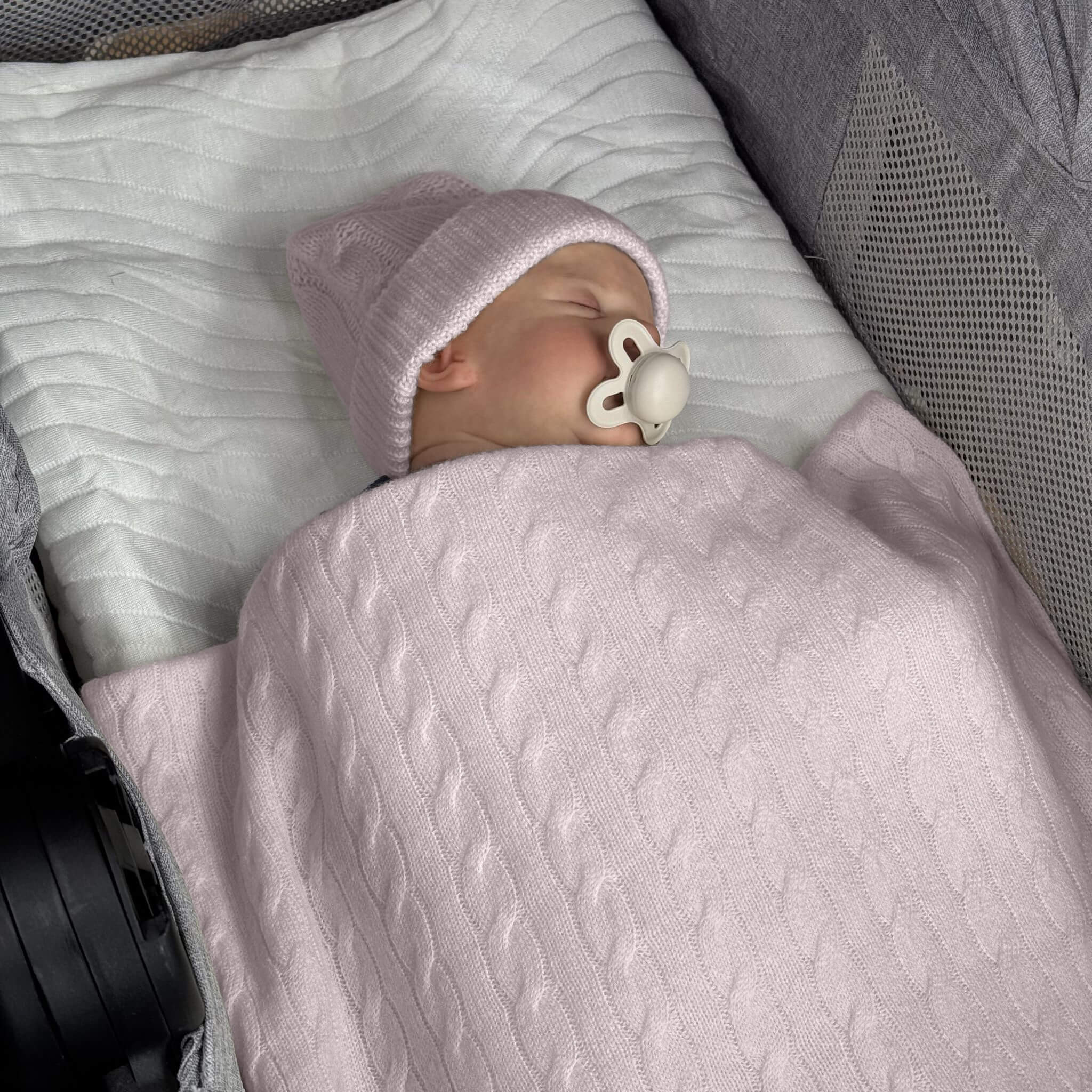 Baby in pram with pink cable knit blanket and pink beanie